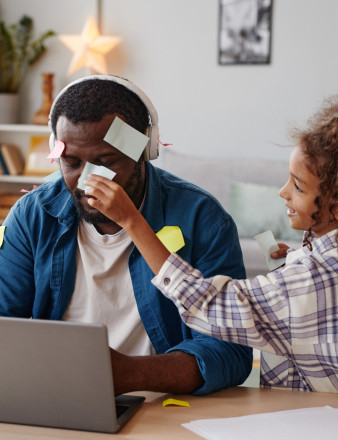 Une petite fille colle des post-il à son papa qui travaille sur un ordinateur portable.